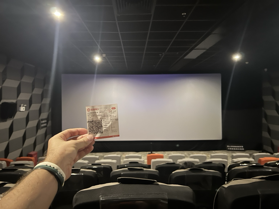 An arm holding out a movie ticket in a mostly empty theater 