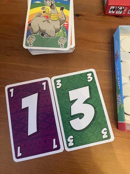 Kartenspiel liegt auf einem Tisch. Aufgedeckt sind die lila 1 und die grüne 3. oberhalb ist die Karte mit dem verrückten Lama zu erkennen.