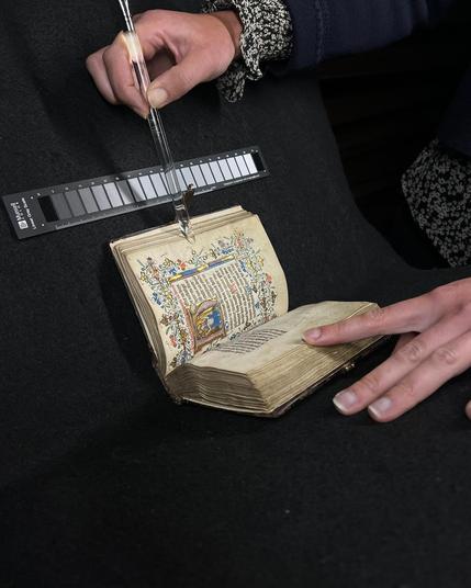 Een middeleeuws manuscript dat voorzichtig opengehouden wordt zodat het gefotografeerd kan worden.