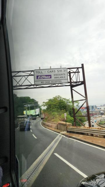 View from inside a bus of a sign over a highway that is descending into a tunnel. Sign reads: 
TOLL - CARS $18.31
EZ PASS DISCOUNTS AVAILABLE 
NO CASH ACCEPTED