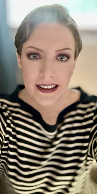 Short brown haired woman w/blue eyes, black and tan stripped shirt, slight smile