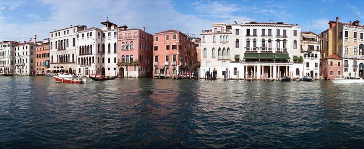 A row of brightly colored buildings lines the edge of a green-gray canal.