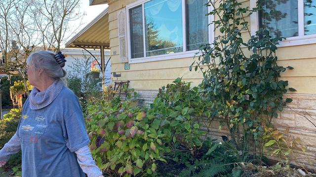 A woman is in front of her house, and she is looking away from the camera. 