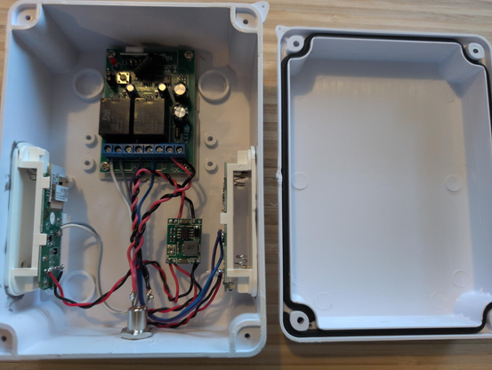 A white project box is opened with the lid to the side. It contains a two channel gate controller, but the momentary contact relays are wired to two Zigbee moisture sensors. The sensor batteries have been removed and they are instead hardwired to a DC-DC buck converter.