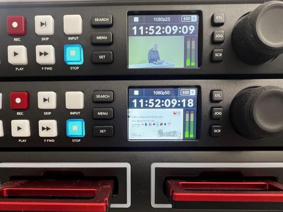 The image shows two digital video recorders with control buttons and small screens. The upper screen displays a person at a table with a green background, while the lower screen shows a document or presentation with text and images. Controls include buttons for recording, playing