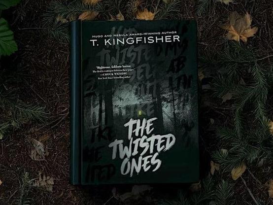The book "The Twisted Ones" laying on the forest floor, next to leaves and twigs.