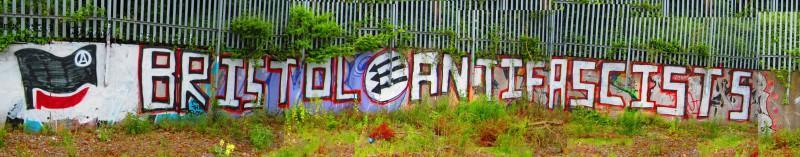 Graffiti reading Bristol Antifascist with the black and red flag and three downward arrows.