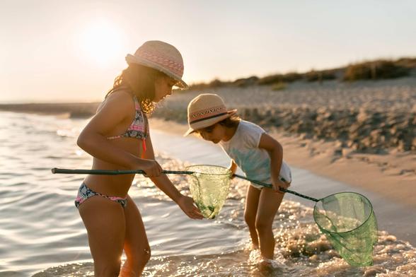 2 young sisters with nets inspecting their finds at the beach.