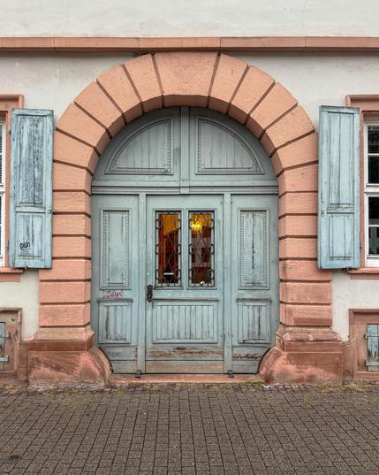 Silbergraues verwittertes rundes Holztor an rosa Sandsteinbogen noch sichtbar sind die anliegenden Fensterläden aus demselben Holz