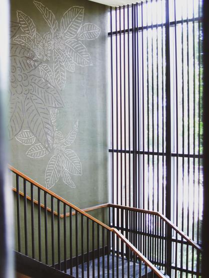 Indoor shot of a staircase with metal railings. It faced floor-to-ceiling windows, while the army green wall is decorated with a simple floral mural.   