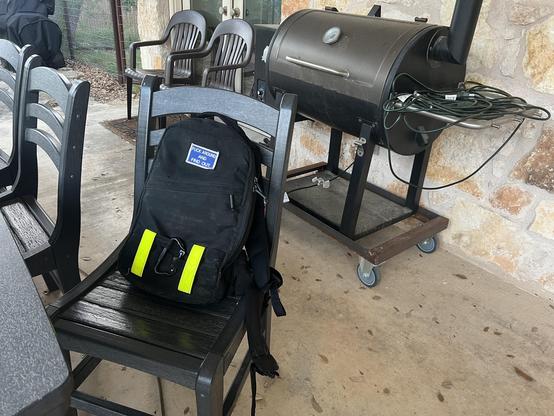 Black rucksack on a chair with a grill in the background. Rucksack has a velcro patch saying "Fuck Around and Find Out"