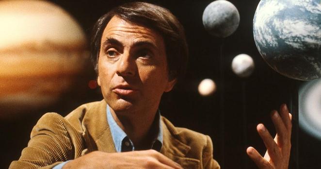 A color photo of scientist and author Carl Sagan, against a backdrop of an image of some of the planets of our solar system.