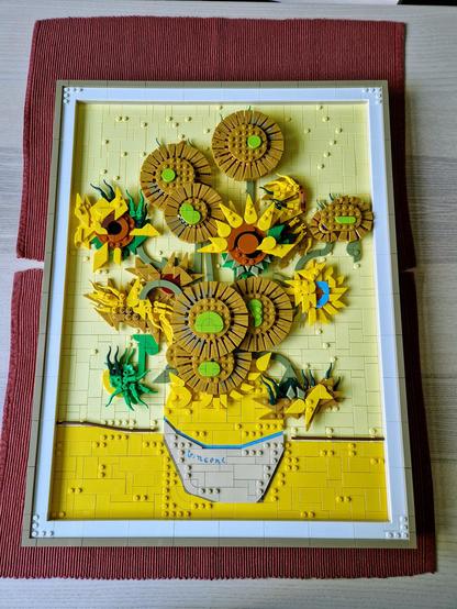 A lego set resembling van gogh's sunflowers paining, laying on a table with dark red placemats underneath.