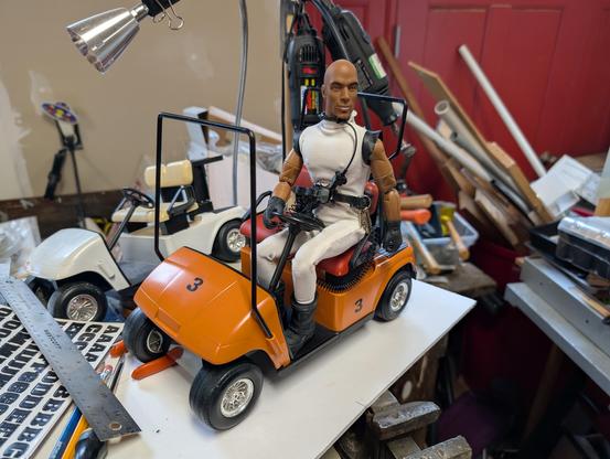 The original white Minionmobile which has served me for years, is in the background. The new one is a modified golf-cart panted a warm orange with redish-brown seats. An action figure in sleeveless white jumpsuit (the Minions At Work uniform) sits in the driver's seat. The new vehicle is marked with the number "3," the universal visual science fiction code for "there are more than one of these, even if we just built one. There are at least three, and if you buy that, there could be a hundred, right?" The joke being that I actually built two.
   The trouble with this is that it looks almost TOO good to fit the MAW aesthetic. I really need to weather and dirty it up. You can also see that I need to cut and extend the metal roof supports about an inch to allow for the larger figure. The seats have already been elevated, and a cutout made in the dash to give a little more foot room. This thing is very undersized, but cramming the larger figures into it gives me a "clown car" feel that plays into the humor of the strip. EVERYTHING the Minions use, from their uniforms to their vehicles, has to be kind of off-spec or inferior in a way that could probably get them killed.
    "Sooner or later, EVERYONE ends up working for the forces of Evil."