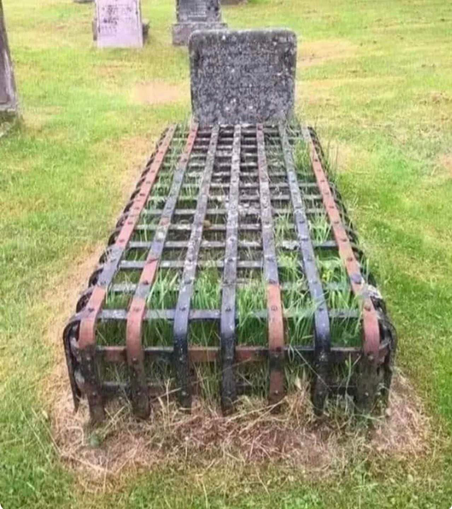 An old grave in a cemetery covered by a heavy metal cage or grate.