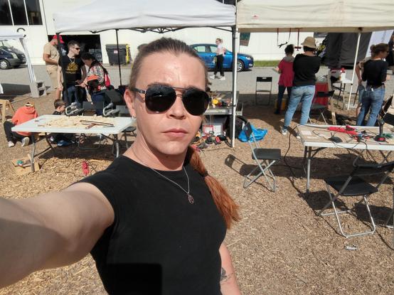 Woman in black tshirt and sunglasses, outdoor workshop area in behind.