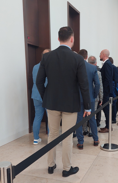 Ausschließlich Männer in blauen business Anzügen stehen am Lift des Humboldt Forums an um zum get together zu gelangen.
