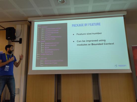 Luigi in front of a projector slide showing a directory tree of PHP files divided by business features, making the distance between logically close related files smaller.