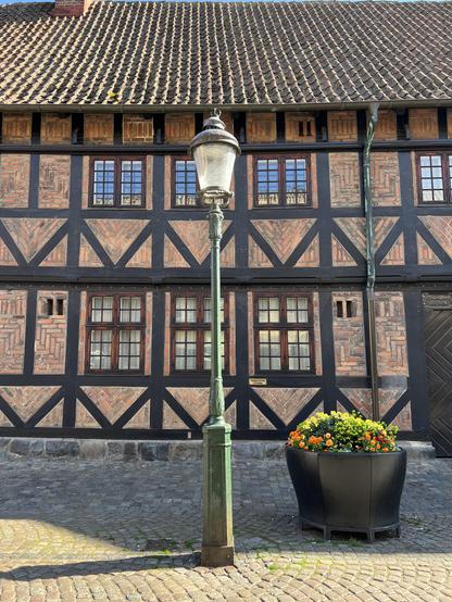 A half-timbered house with an old lantern out on the cobbled street and a pot with flowers.