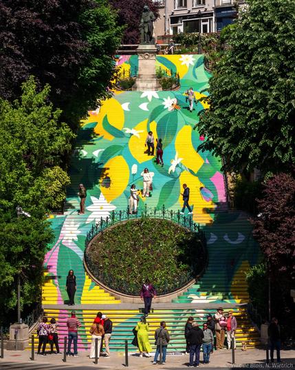 Photo d’ensemble de l’escalier Denis-Papin, dont les contre-marches sont recouvertes pour former un décor graphique de citrons, de feuilles et de petits insectes. Des personnes montent l’escalier et donnent l’illusion de marcher à travers la végétation.