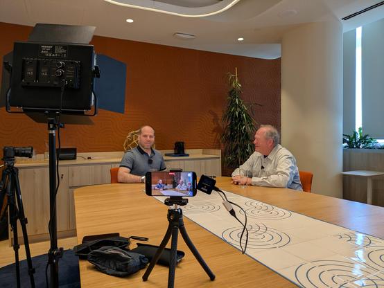 Geoff Huston being interviewed at the Cloudflare office in Lisbon, from behind the cameras. There are a few cameras and lights visible.