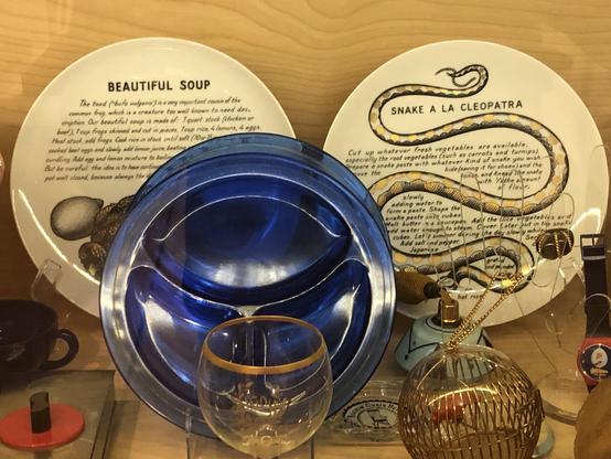 A decorative plate that says "Beautiful Soup" next to a plate that says "Snake a la Cleopatra" and shows a snake. Each has a recipe on it I think.
