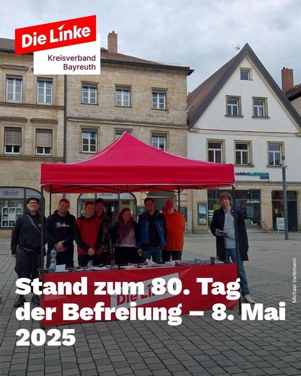 Das Bild zeigt einen Informationsstand von Die Linke Kreisverband Bayreuth auf einem öffentlichen Platz. Der Stand besteht aus einem roten Pavillon und einem Tisch mit Flyern. Mehrere Mitglieder der Partei stehen freundlich dahinter und lächeln in die Kamera. Im Hintergrund sind historische Gebäude zu sehen. Auf dem Bild steht die Überschrift: „Stand zum 80. Tag der Befreiung – 8. Mai 2025“.
