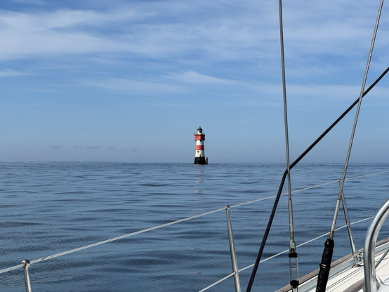 In etwas weiterer Ferne der Leuchtturm inmitten der spiegelnden Nordsee. Im Vordergrund die Wanten und der Seezaun der Segelyacht „Polaris“.