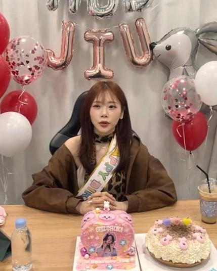 screenshot of jiu (dreamcatcher) during her birthday livestream. ballons in the back. birthday cakes on the table in the front.