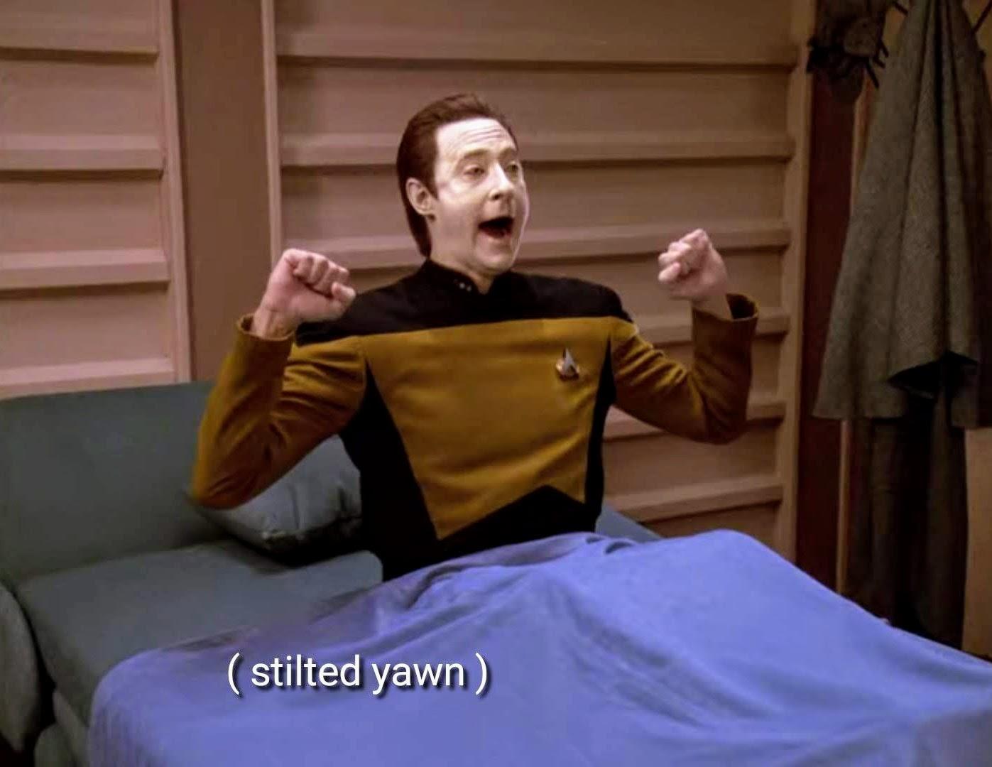 Star Trek The Next Generation scene. We're in the bedroom of Data's personal quarters. He's in full starfleet uniform sitting up in a bed and yawning with arms stretching (or as I would say to my dogs "BIG STRETCH"). A blankie is pulled up over him up to the waist. Closed caption reads, "(stilted yawn)"