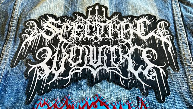 A Spectral Wound patch freshly sewn on the back of a blue denim jacket.  