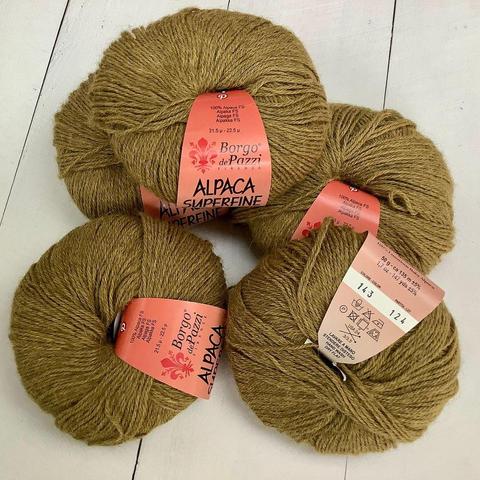 A pile of 5 balls of mustard-yellow yarn, on a white plank background. 