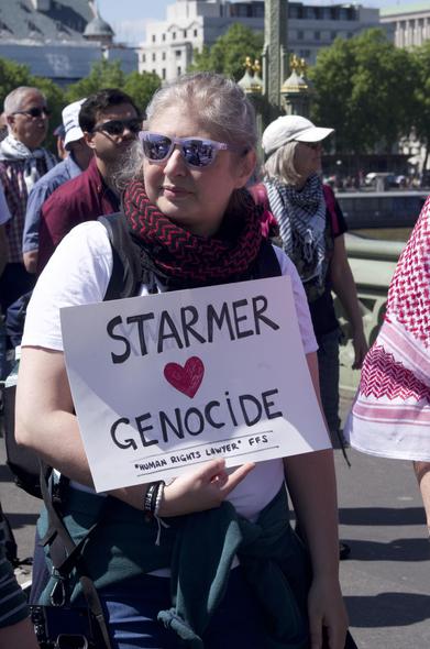 woman carrying sign 'Starmer HEARTEMOJI genocide'
