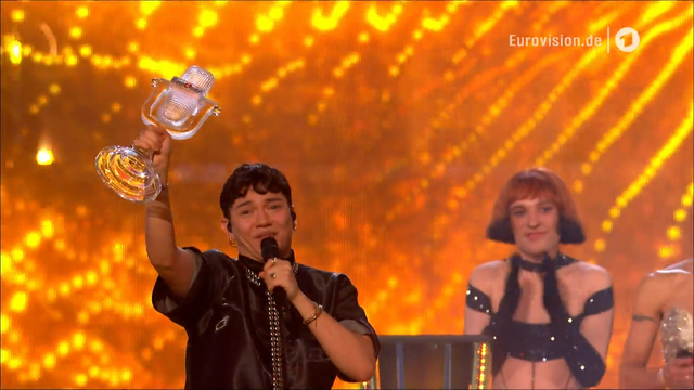 JJ nimmt die Trophäe für den Gewinn des ESC 2025 entgegen und hält das gläserne Mikrofon dankbar und freudig in der Luft.