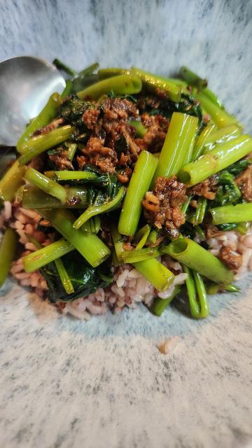In a bowl is a serving of brown rice topped with sauteed water spinach cooked with lots of garlic and some corned tuna