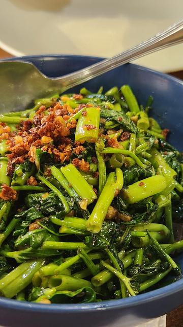 On a blue serving plate is water spinach topped with lots of toasted garlic