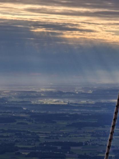 View of Bavaria from a hot air balloon. The sunlight is slanting through clouds over a green and grey landscape.