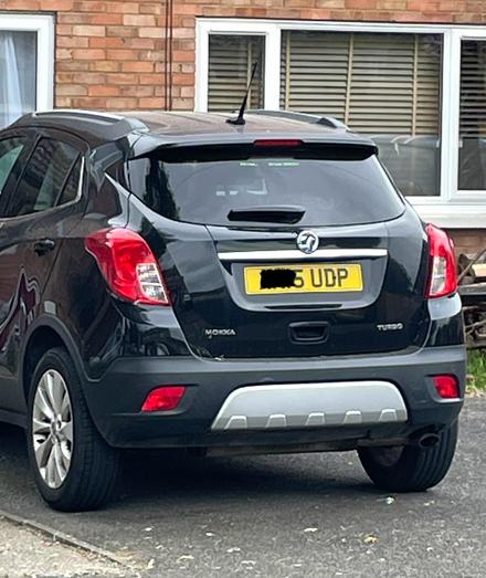 A small black car on a driveway which has a number plate ending in UDP.