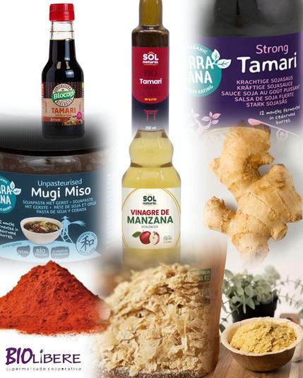 La imagen muestra una variedad de ingredientes alimenticios, incluyendo dos tipos de salsa de soja tamari (una oscura y otra clara), miso de cebada sin pasteurizar, vinagre de manzana, jengibre fresco, pimentón rojo molido y levadura nutricional. Todos los productos parecen ser orgánicos y de alta calidad, mostrando sus etiquetas en varios idiomas. La imagen está compuesta para parecer una colección de ingredientes para una receta.