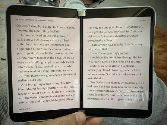 Close up of a hand holding a Surface Duo 2, a dual-screened, folding smartphone, displaying two pages from the e-book Artificial Condition.