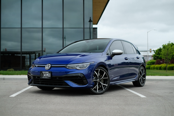 A blue sporty hatchback parked in front of a glass building 