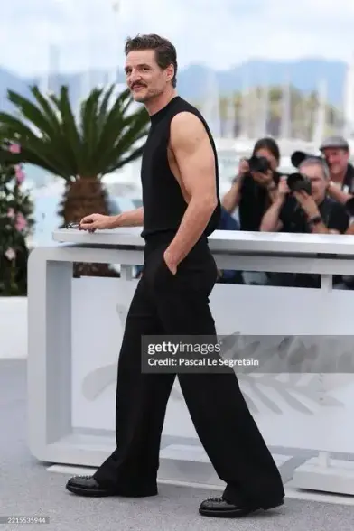 Pedro Pascal in Cannes. He wears all black trousers, shoes and a muscle shirt without arms that show off his biceps.
