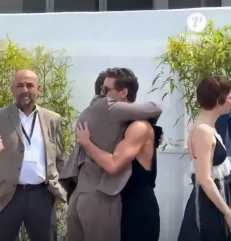Pedro Pascal in Cannes. He wears all black trousers, shoes and a muscle shirt without arms that show off his biceps. He hugs a fellow other actor.