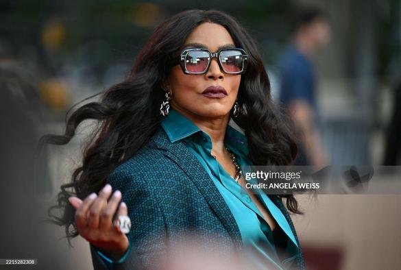 Angela Bassett in a green suit with a green silk blouse. She wears long open black hair and a big sun glasses.