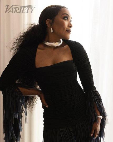 Angela Bassett in photoshoot for Variety in her outfit she wore on the red carpet in Cannes. It's a black form-fitting dress with  bolero jacket with long chiffon trumpet sleeves. She wears her long black hair in a curly ponytail and silver jewelry.