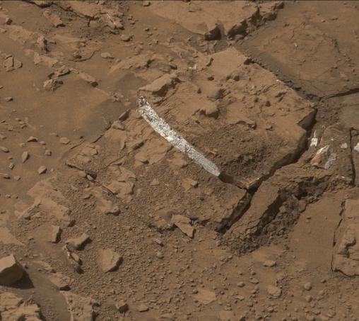 A rust toned image of a broken Martian rock, revealing a bright white interior.