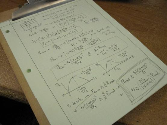 An engineer's pad showing a computation for a particular LED circuit. On a wooden chipboard clipboard and a wooden desk.