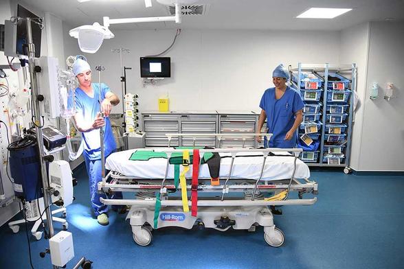 Deux soignants en tenue de bloc préparent une salle de déchocage moderne à l’Hôpital Nord, autour d’un lit médicalisé équipé de harnais de maintien colorés, dans un environnement technique neuf et organisé.