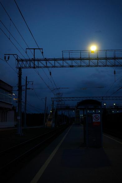 Late evening. Peron of a railroad station. Railroad track. From above you can see a number of metal trusses. On one of them shines a lantern that looks like the moon.