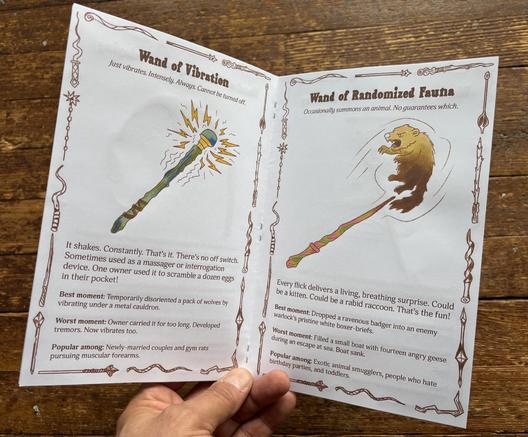 a hand holds a zine open to ‘Wand of Vibration’ on one page and ‘Wand of Randomized Fauna’ on the other.